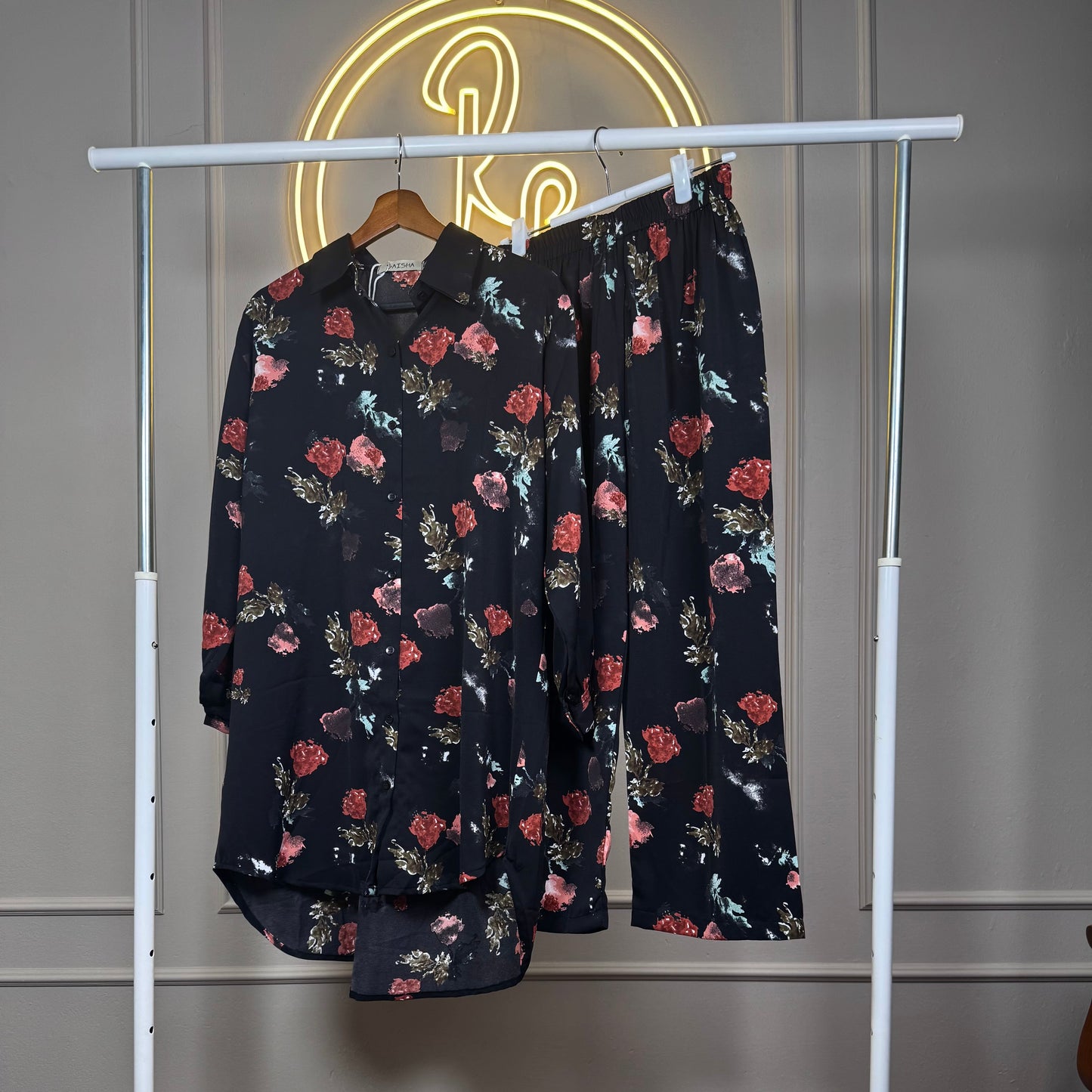 Floral-patterned shirt and pants on a white rack against a neutral wall.