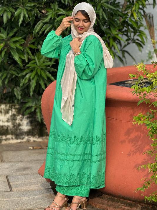 Woman in a green embroidered dress standing next to a large pot with plants.