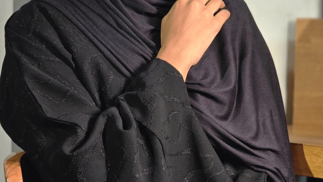 Person wearing black jacquard abaya and a black jersey hijab with a blurred background