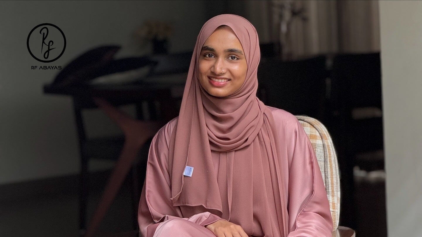 Woman wearing a pink tiktok abaya sitting in a room with blurred background